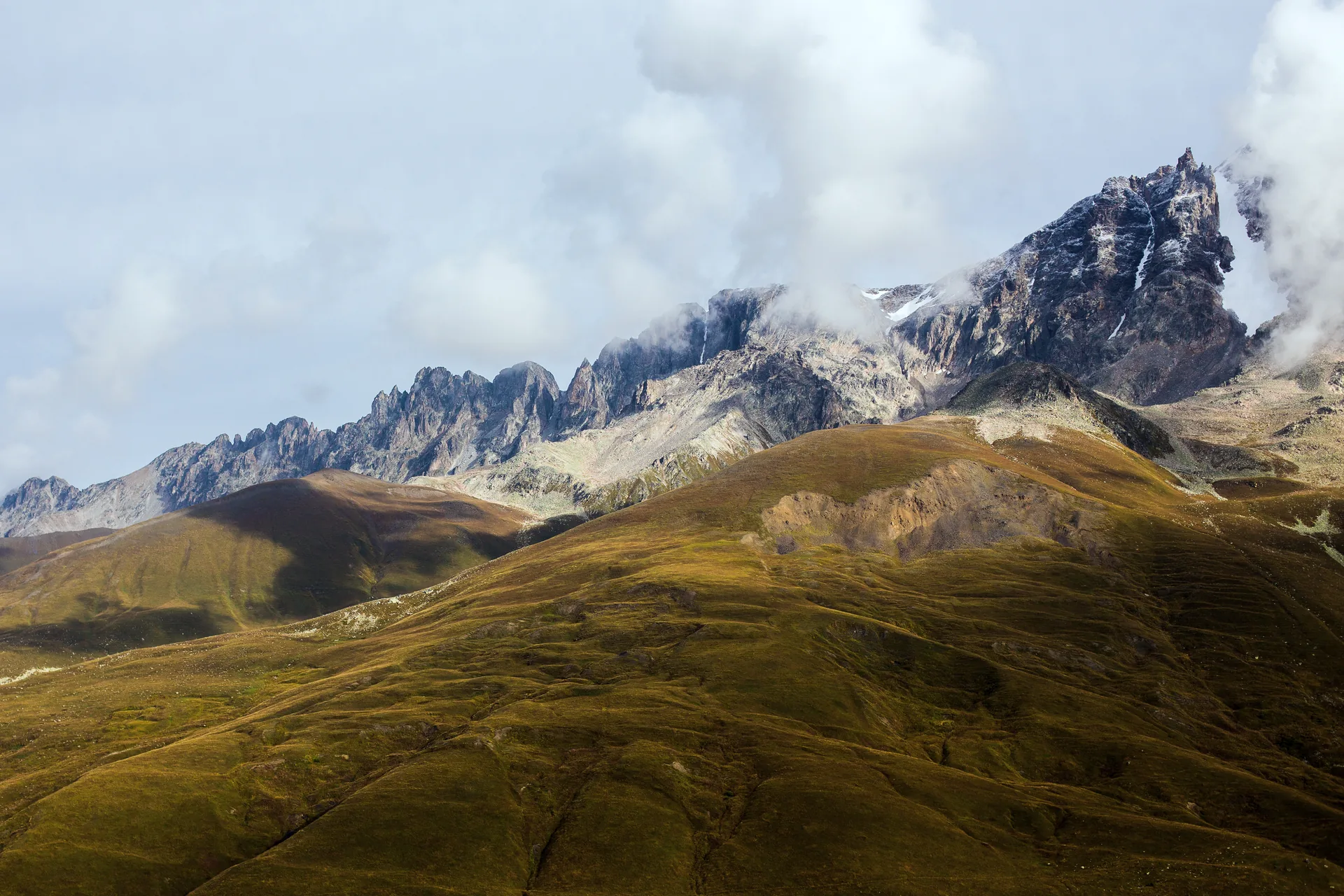Golden autumn grass on rounded slopes under a jagged grey ridge of the Caucasus
