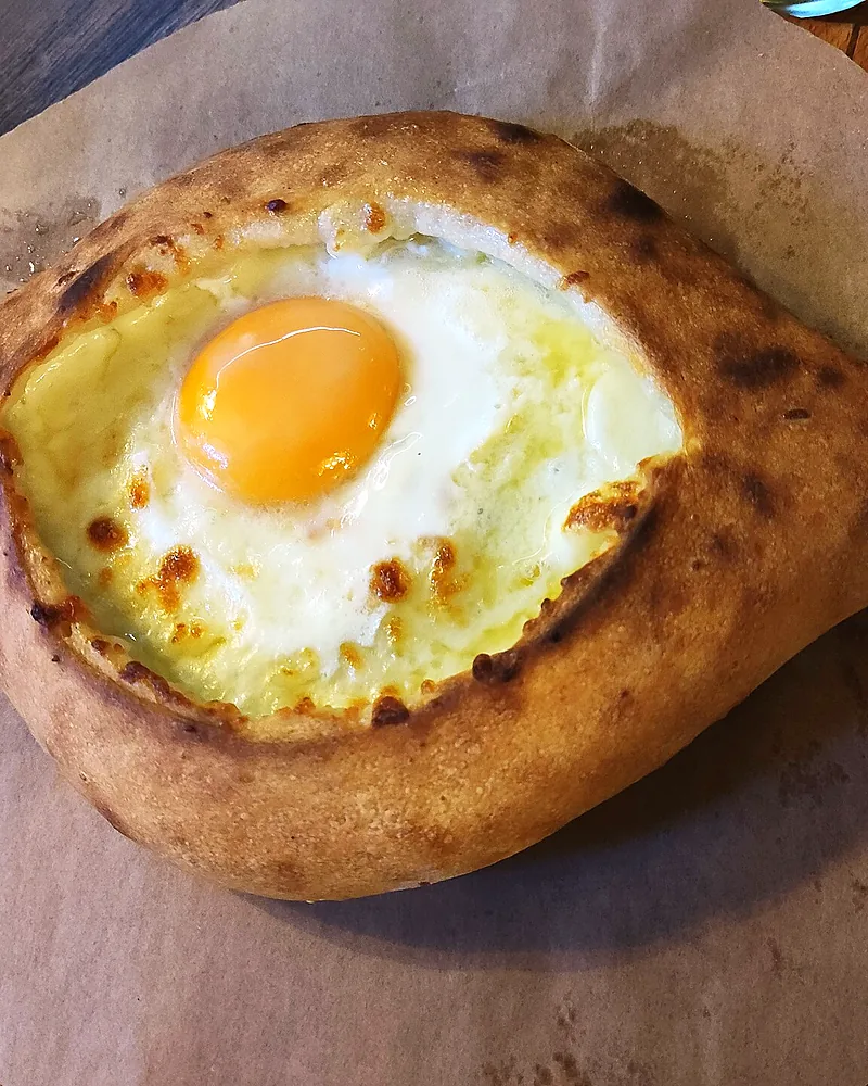 An Adjaruli khachapuri boat on baking paper, the yolk whole in the middle of the cheese
