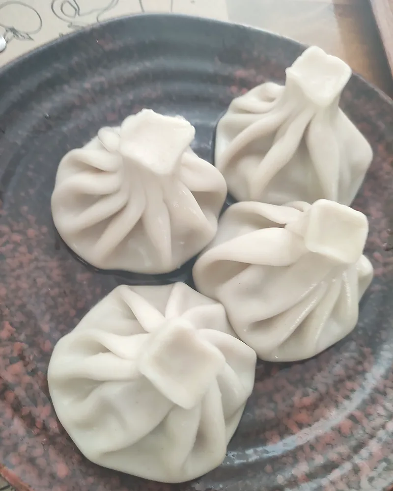Four khinkali on a speckled clay plate, the pleats sharp and the tops twisted