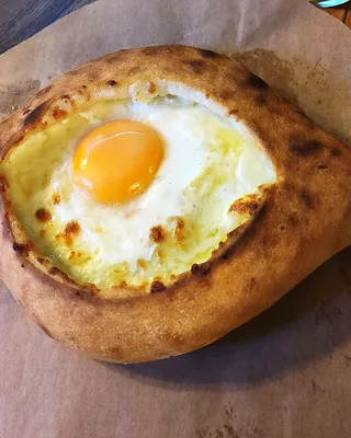 An Adjaruli khachapuri boat on baking paper, the yolk whole in the middle of the cheese