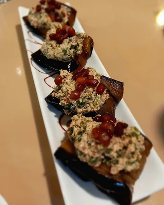 Rolls of fried aubergine filled with walnut paste and topped with pomegranate on a long white plate