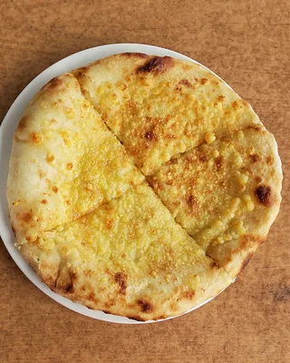 A round Imeruli khachapuri cut into quarters on a white plate, seen from above