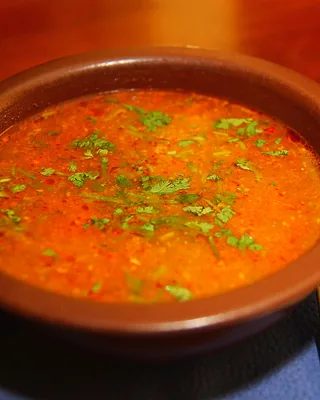 A clay bowl of red kharcho soup with coriander scattered on top