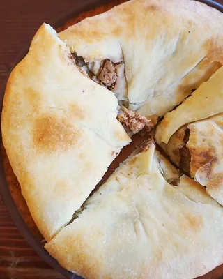A round lobiani, bread filled with beans, cut into quarters on a clay plate