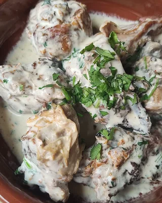 Shkmeruli, chicken in a garlic and milk sauce, in a clay pan with chopped herbs