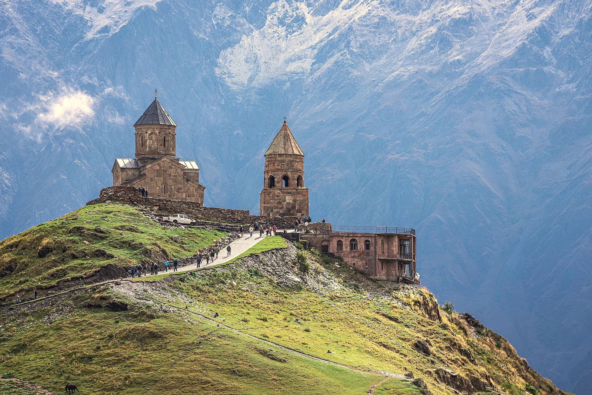 Gergeti Trinity Church on its green hill, the grey rock wall of the Kazbek massif filling the sky behind it