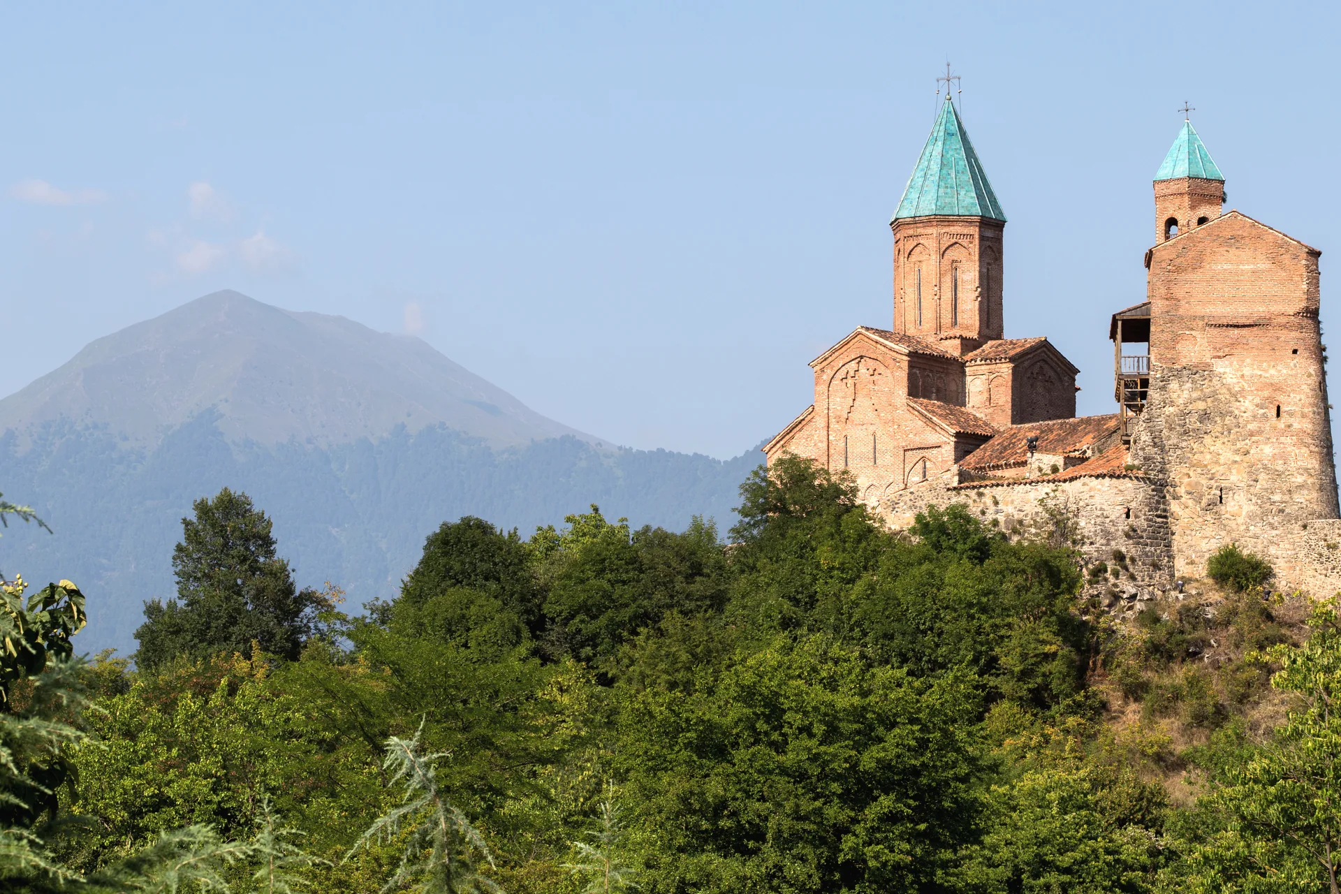 The brick church and tower of Gremi above the trees, a mountain behind in haze
