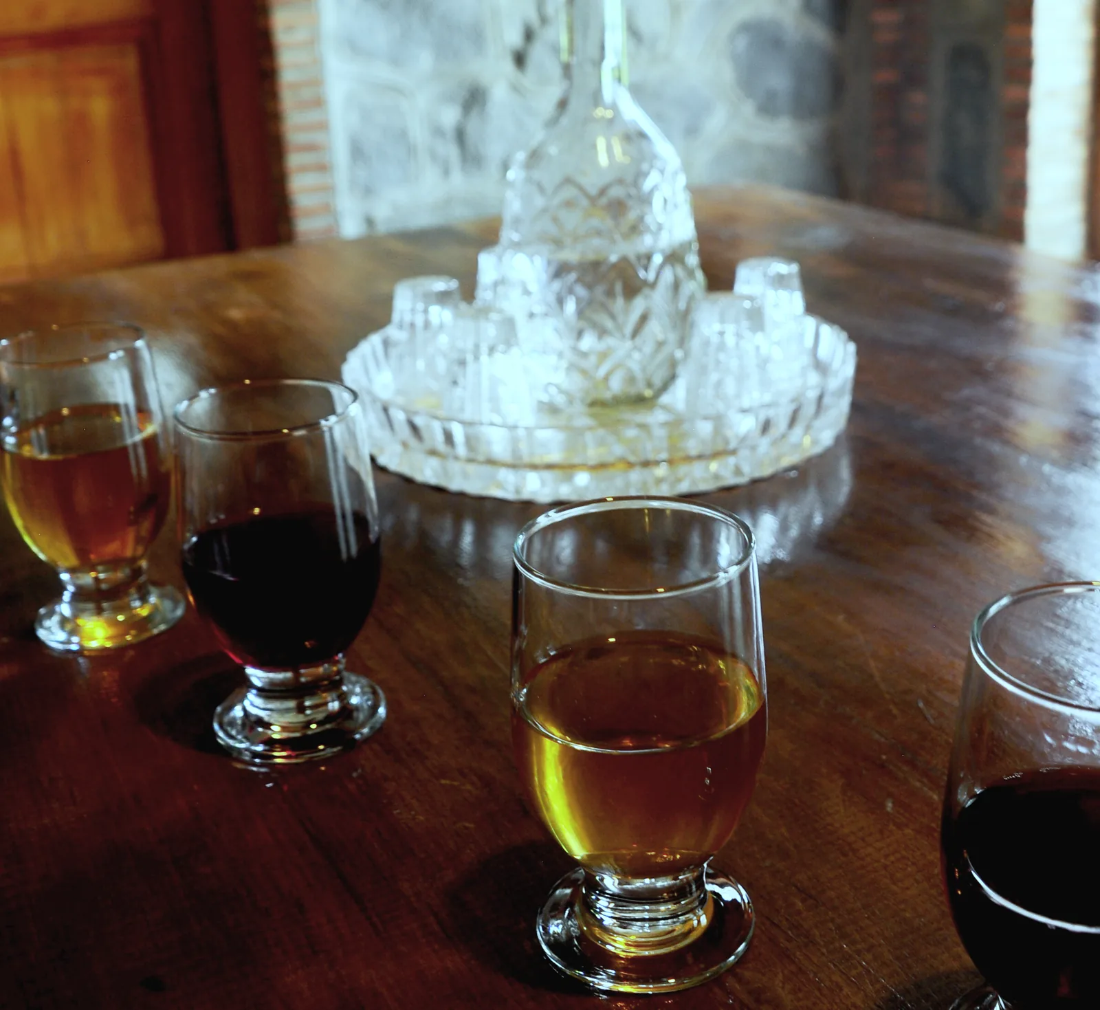 Small glasses of amber and red wine on a dark wooden table, a crystal carafe behind, at Tsinandali