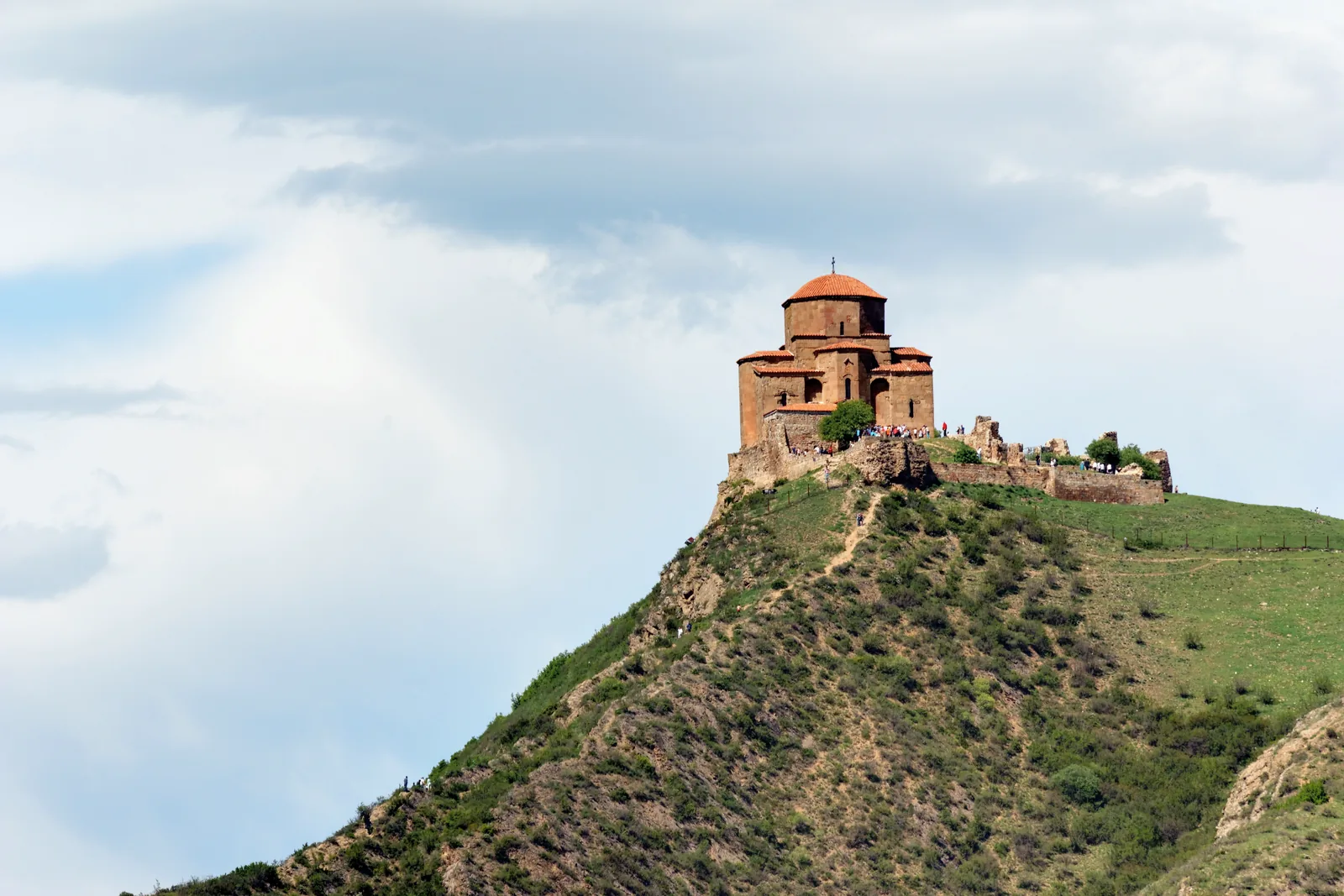 Jvari monastery alone on its green rocky spur under a wide cloudy sky