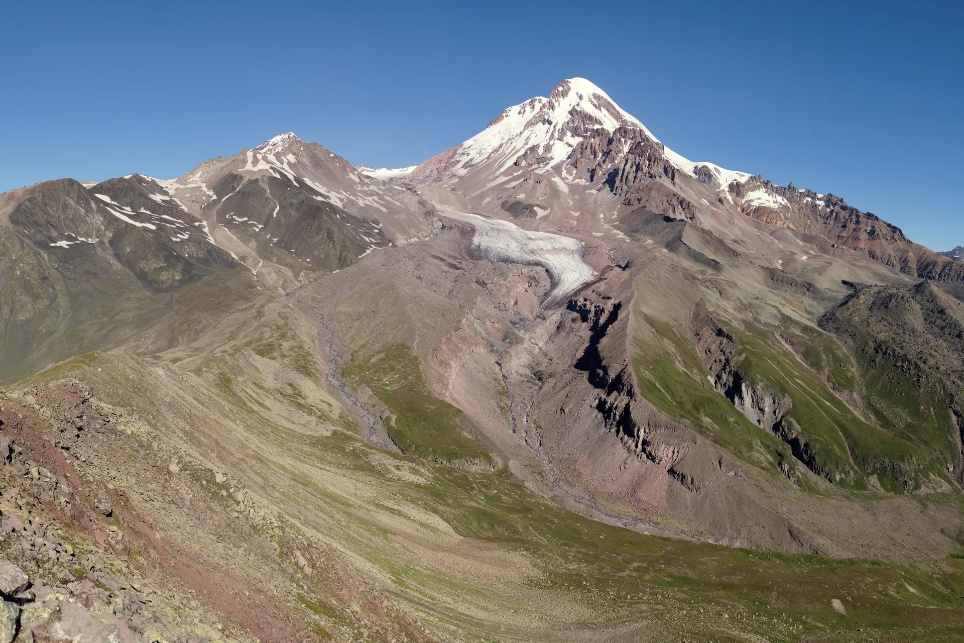 Mount Kazbek with the Gergeti glacier running down its flank, bare brown ridges below