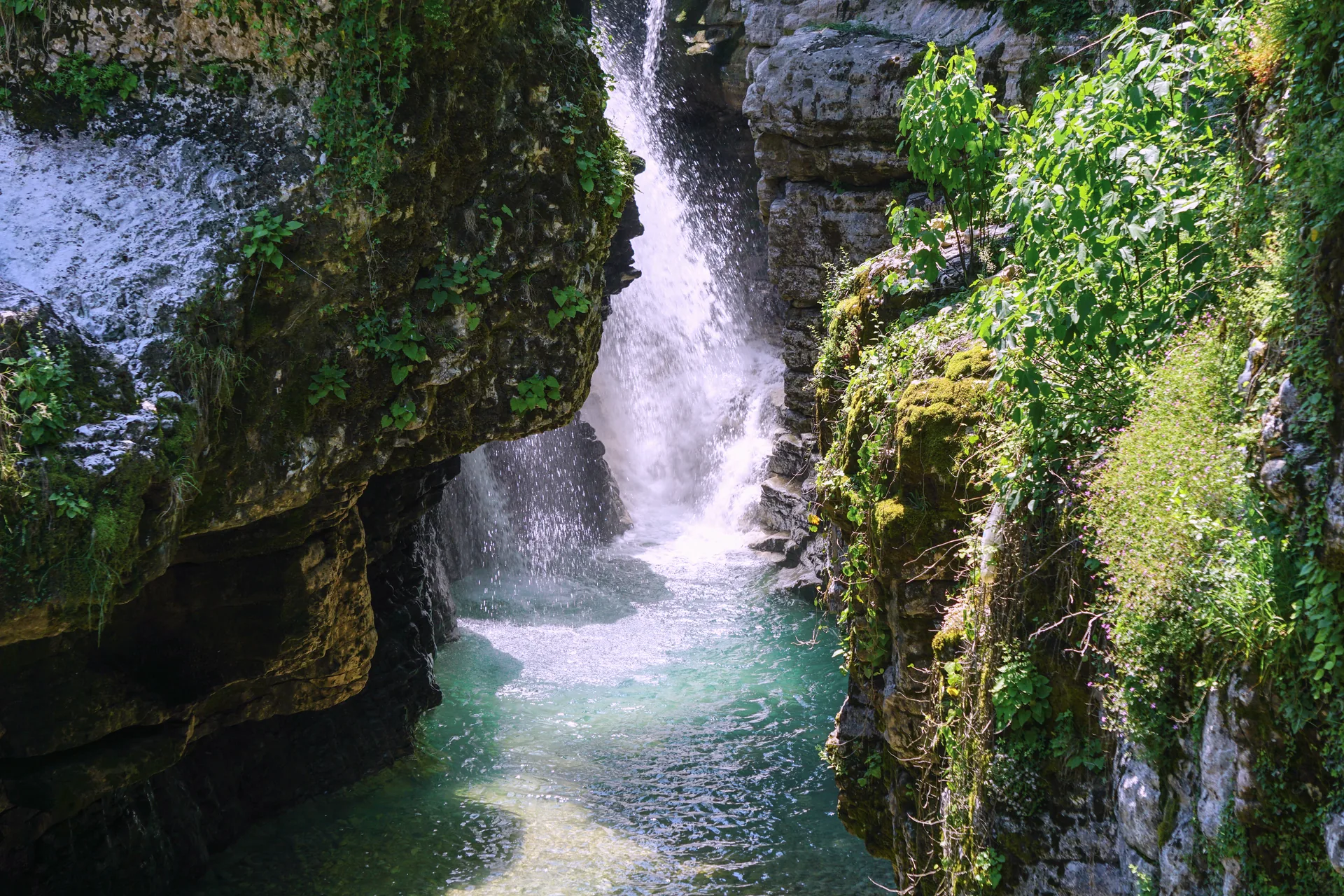 A waterfall falling into a green-blue pool between mossy walls of the Martvili canyon