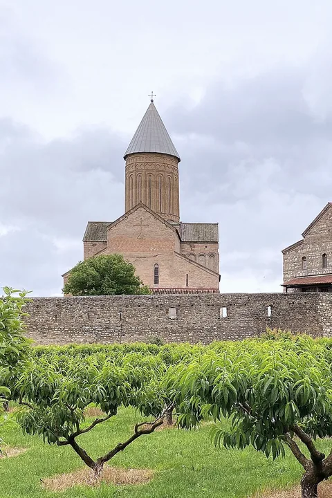 Alaverdi cathedral with its tall drum above a stone wall and a green orchard