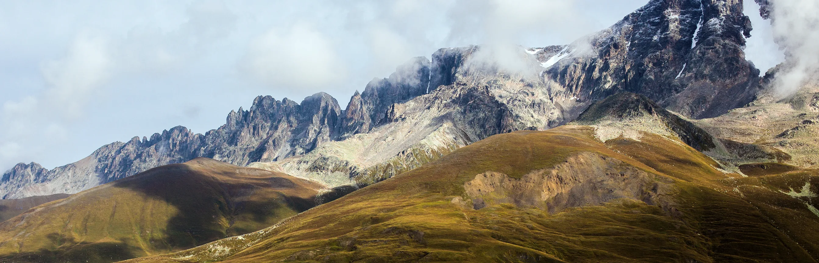 Golden autumn grass on rounded slopes under a jagged grey ridge of the Caucasus