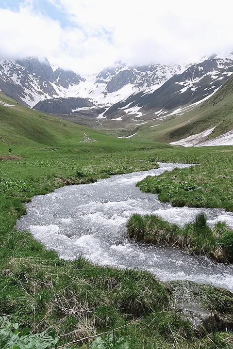 A river winding through the green Juta valley under snow peaks