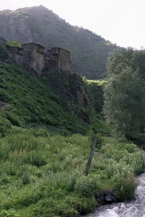 The stone towers of Shatili on a green slope above a rushing river