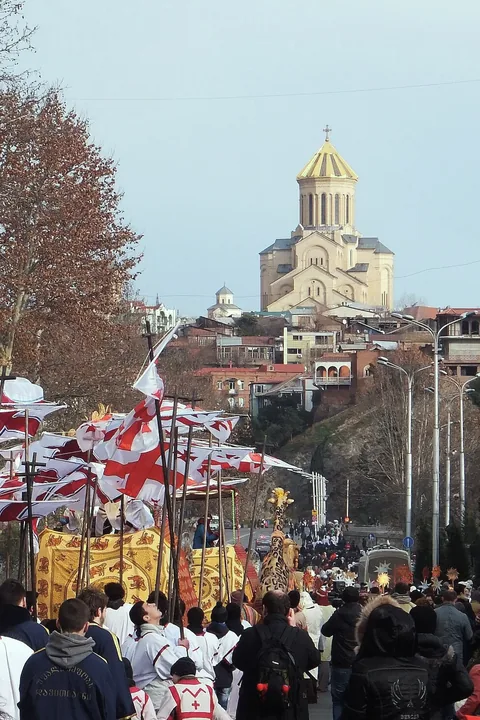 Crowds with red and white flags in the Alilo procession, Sameba cathedral above the old town
