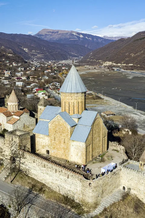The walled Ananuri fortress and its domed church above a pale reservoir, snow on the ridges beyond