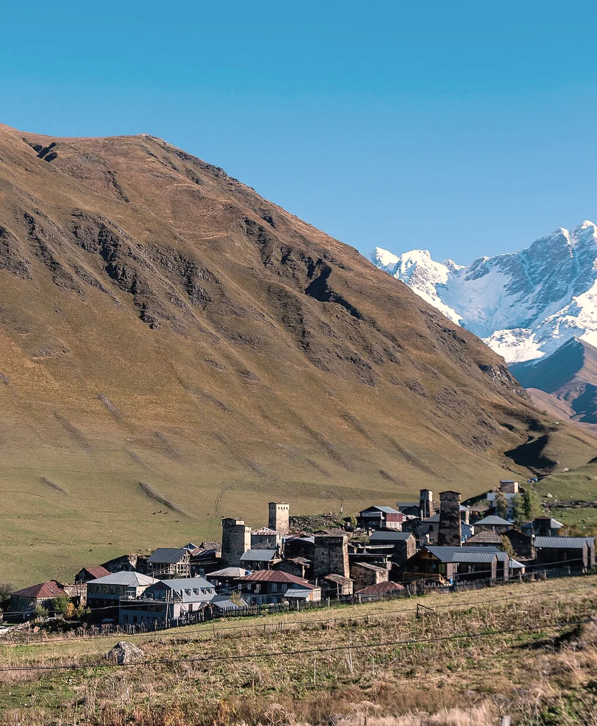 The stone towers of Ushguli below a brown ridge, the snow of Shkhara behind