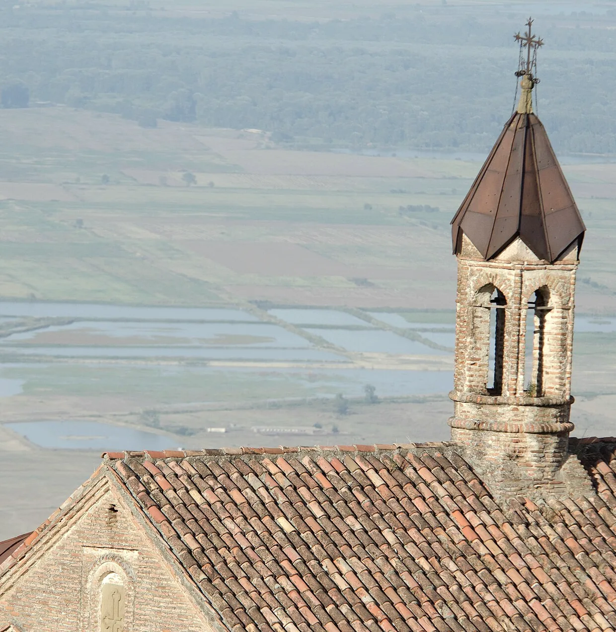 The bell tower and tiled roof of a Sighnaghi church, the Alazani plain far below in evening haze