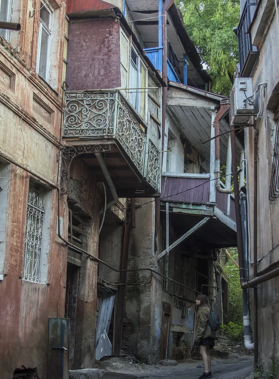 A narrow lane in old Tbilisi, wooden balconies stacked above it and one person walking through