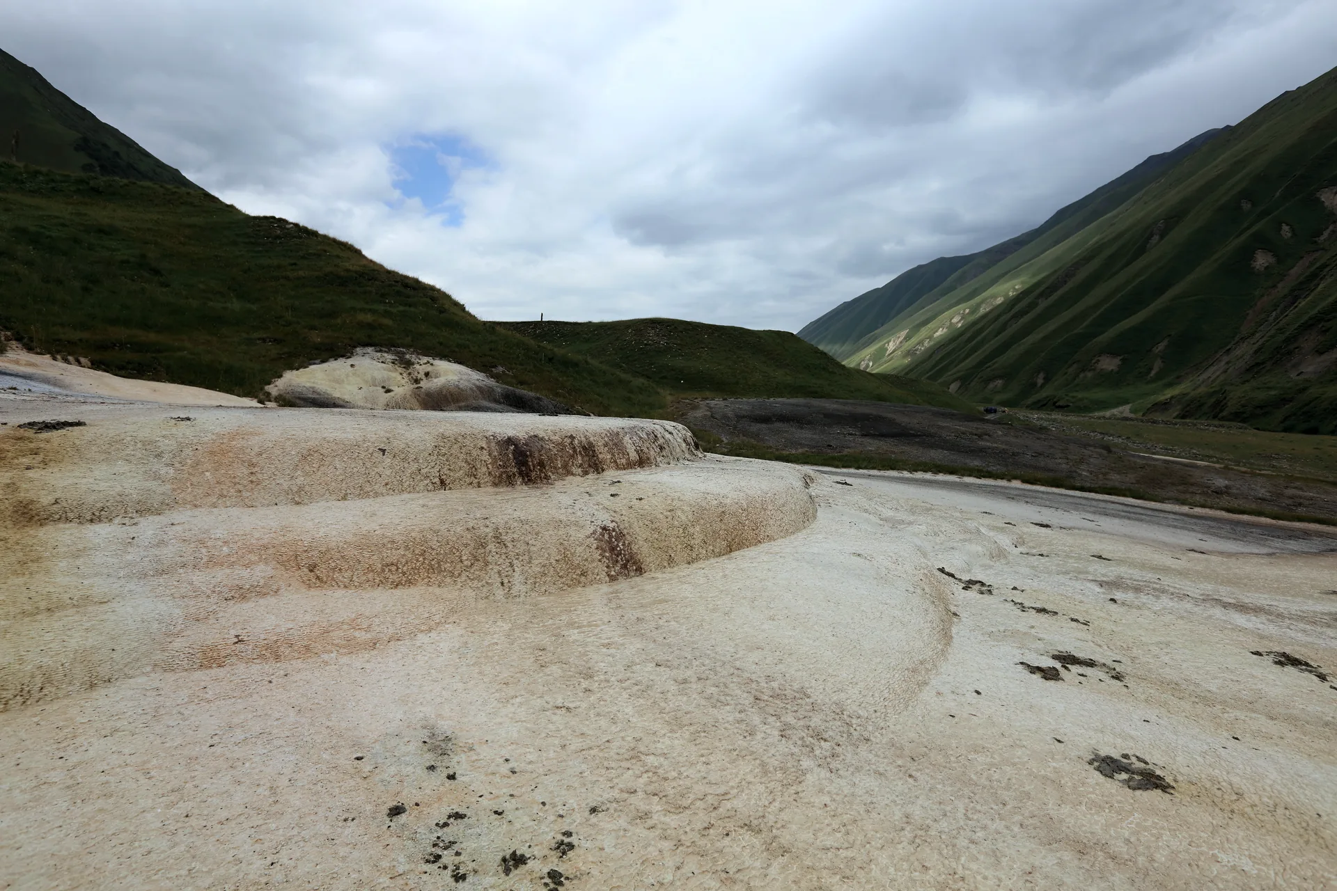 Pale travertine terraces on the floor of the Truso valley, green slopes and cloud behind