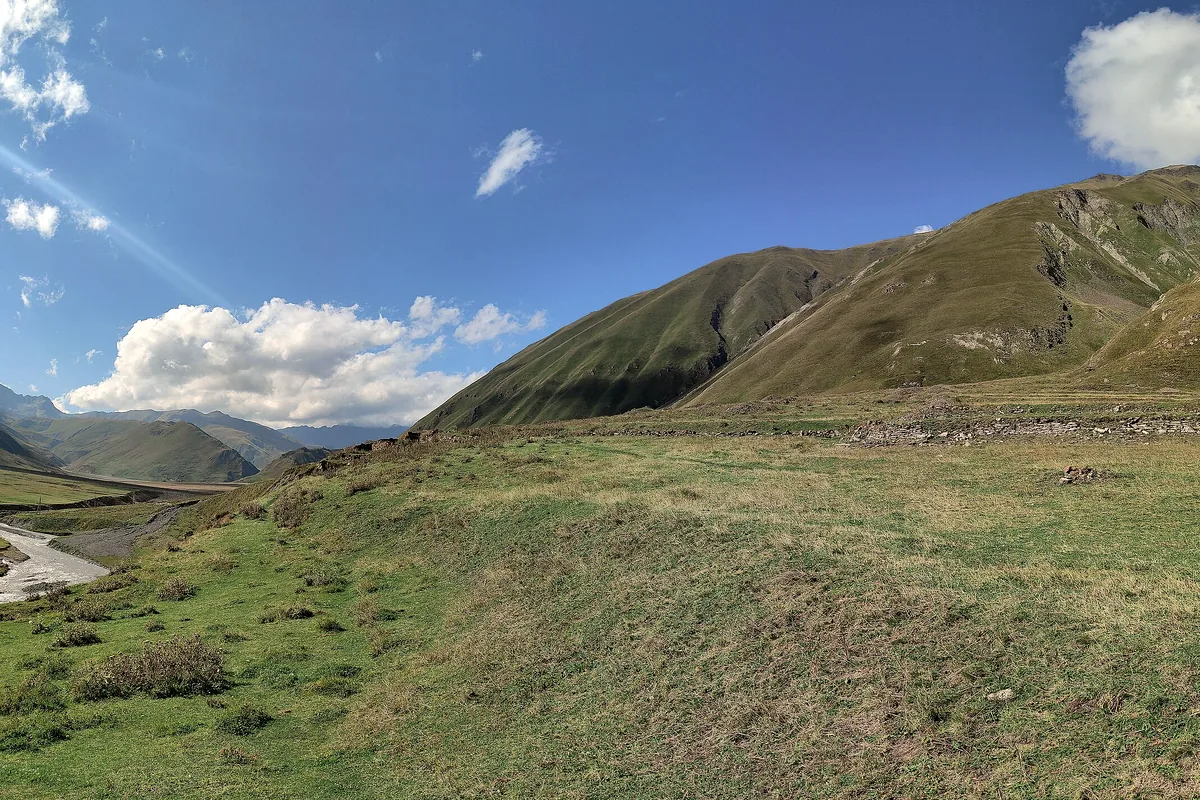 A green upland valley with a track along the river under bare ridges, Truso, Kazbegi